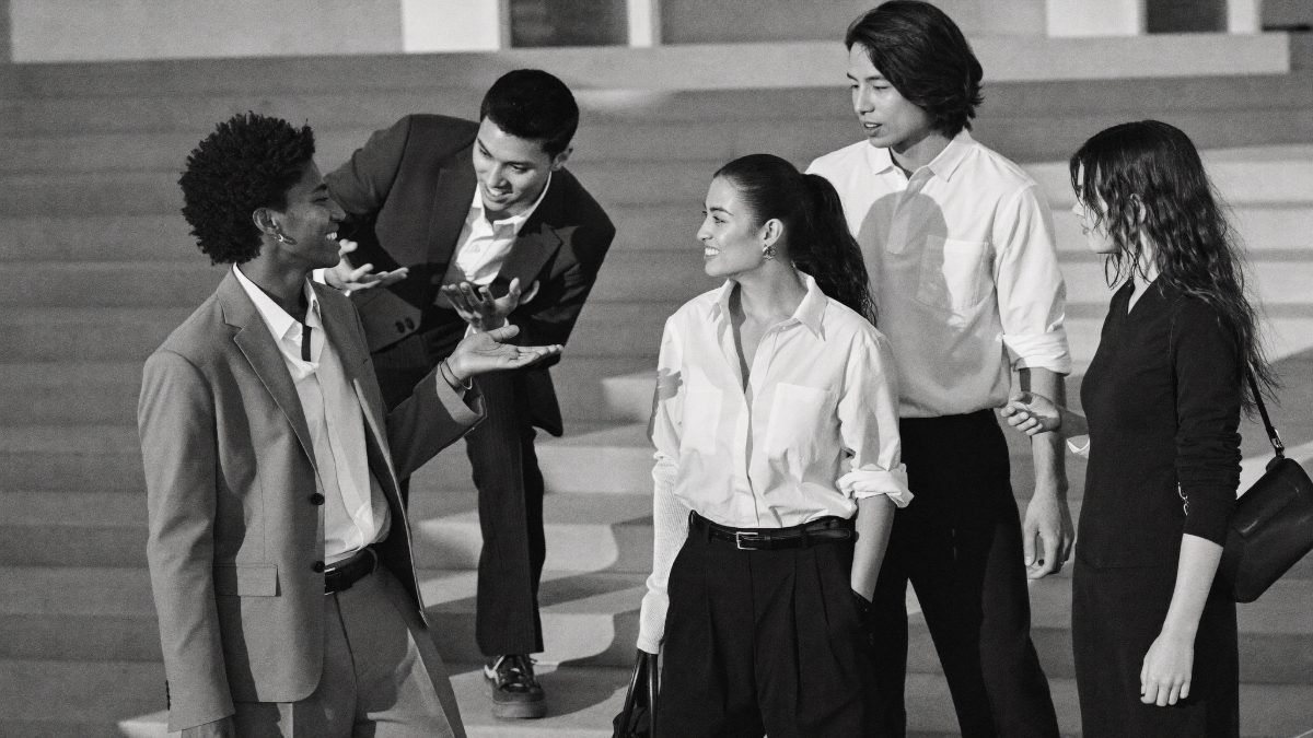 Five young people talking and laughing together on wide steps, one explaining an idea with their hands.