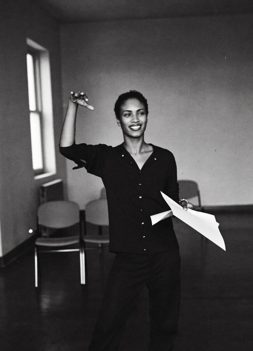 A founder rehearses her pitch alone in an empty room, one hand raised mid-gesture, notes in the other.